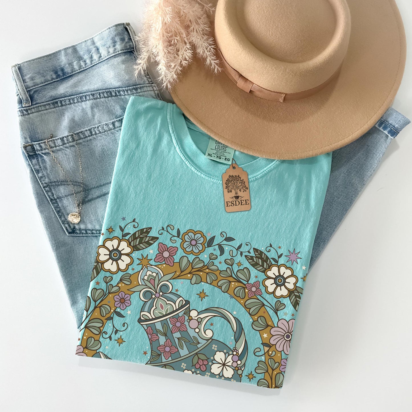 Light blue t-shirt with floral design, denim jeans, and beige hat on a white background