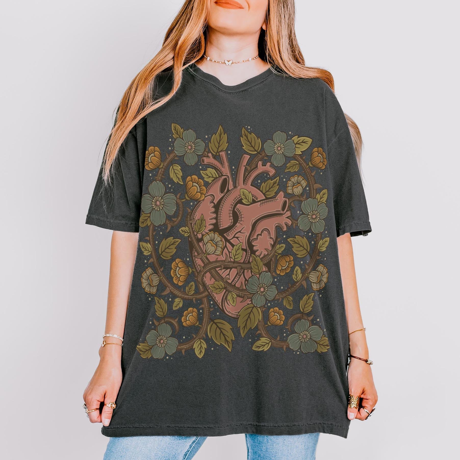 Person wearing a dark gray t-shirt with a floral and anatomical heart design on a plain background Esdee