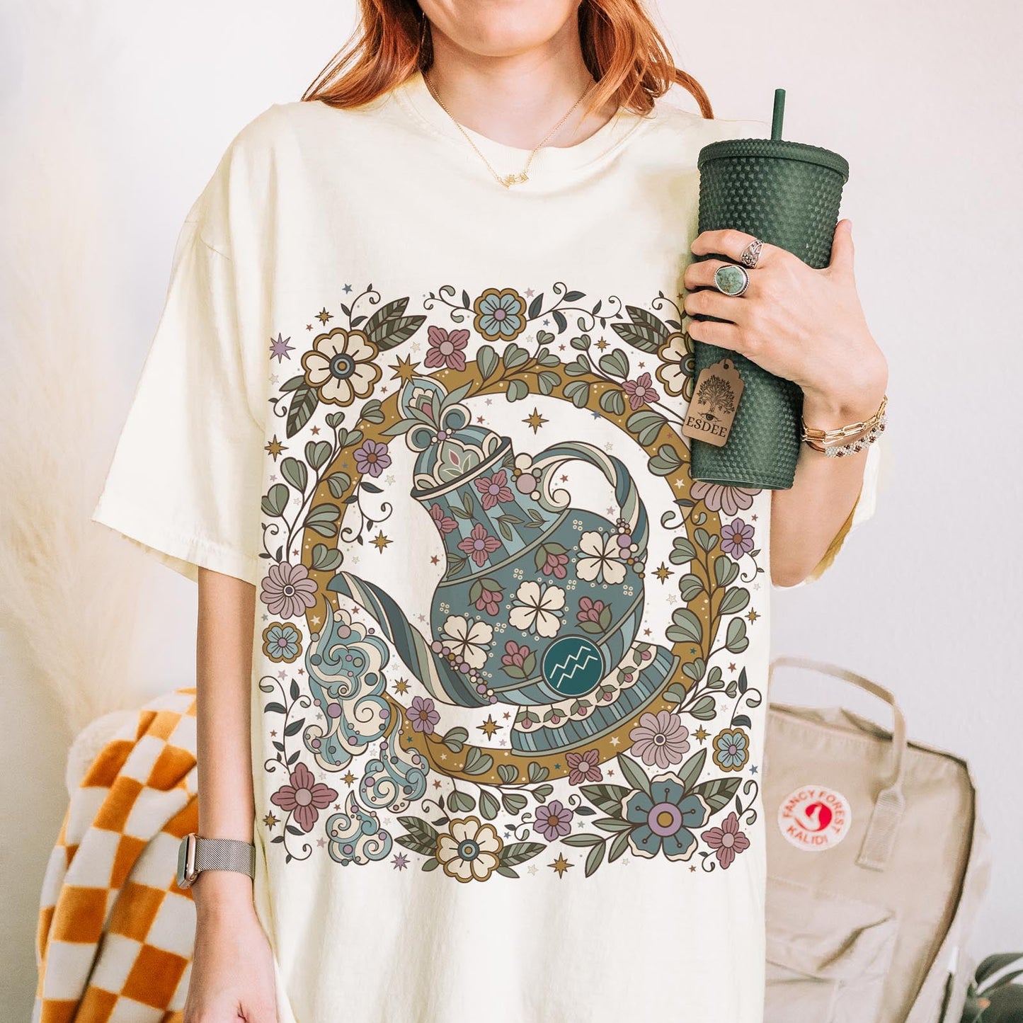 Person wearing a white t-shirt with a decorative cat design, holding a green cup.