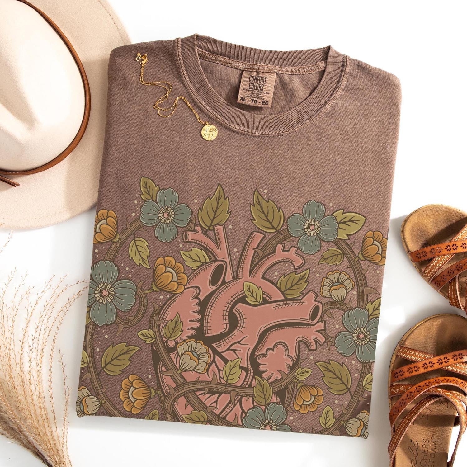 Brown t-shirt with floral and heart design, beige hat, and sandals on a white background