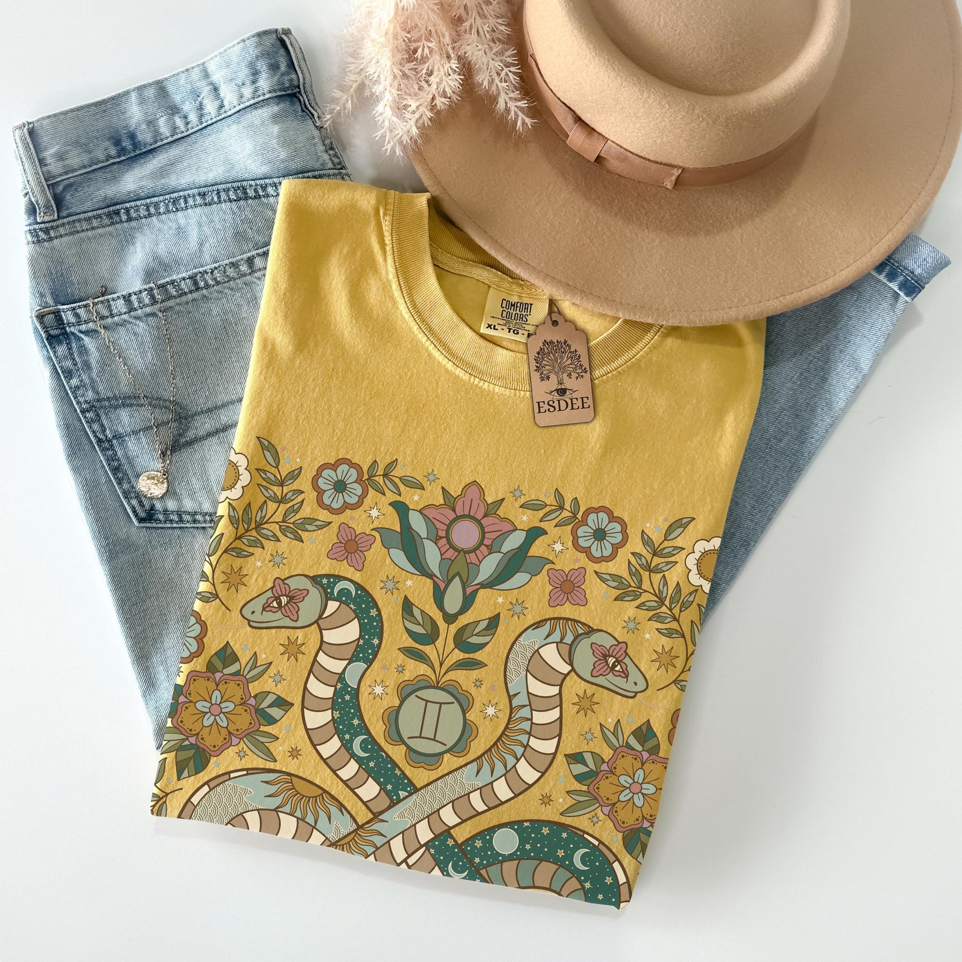 Yellow t-shirt with snake and floral design, denim jeans, and beige hat on a white background
