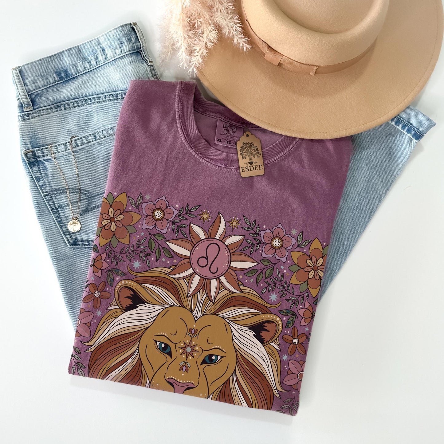 Purple t-shirt with lion design, denim jeans, and beige hat on a white background