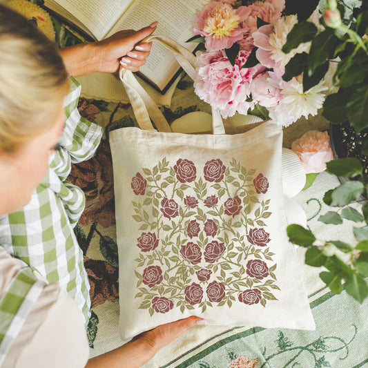 Person holding a tote bag with floral design next to flowers
