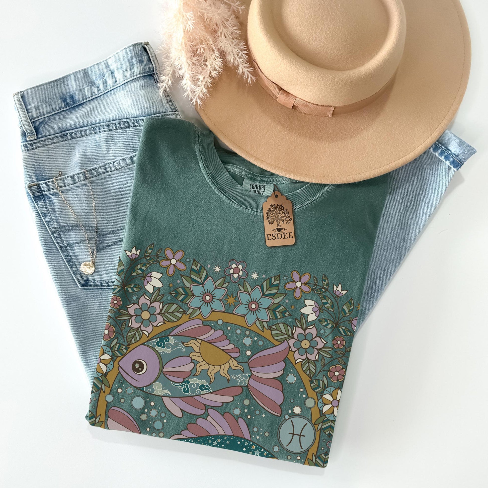 Teal t-shirt with floral and fish design, paired with denim jeans and a beige hat on a white background.