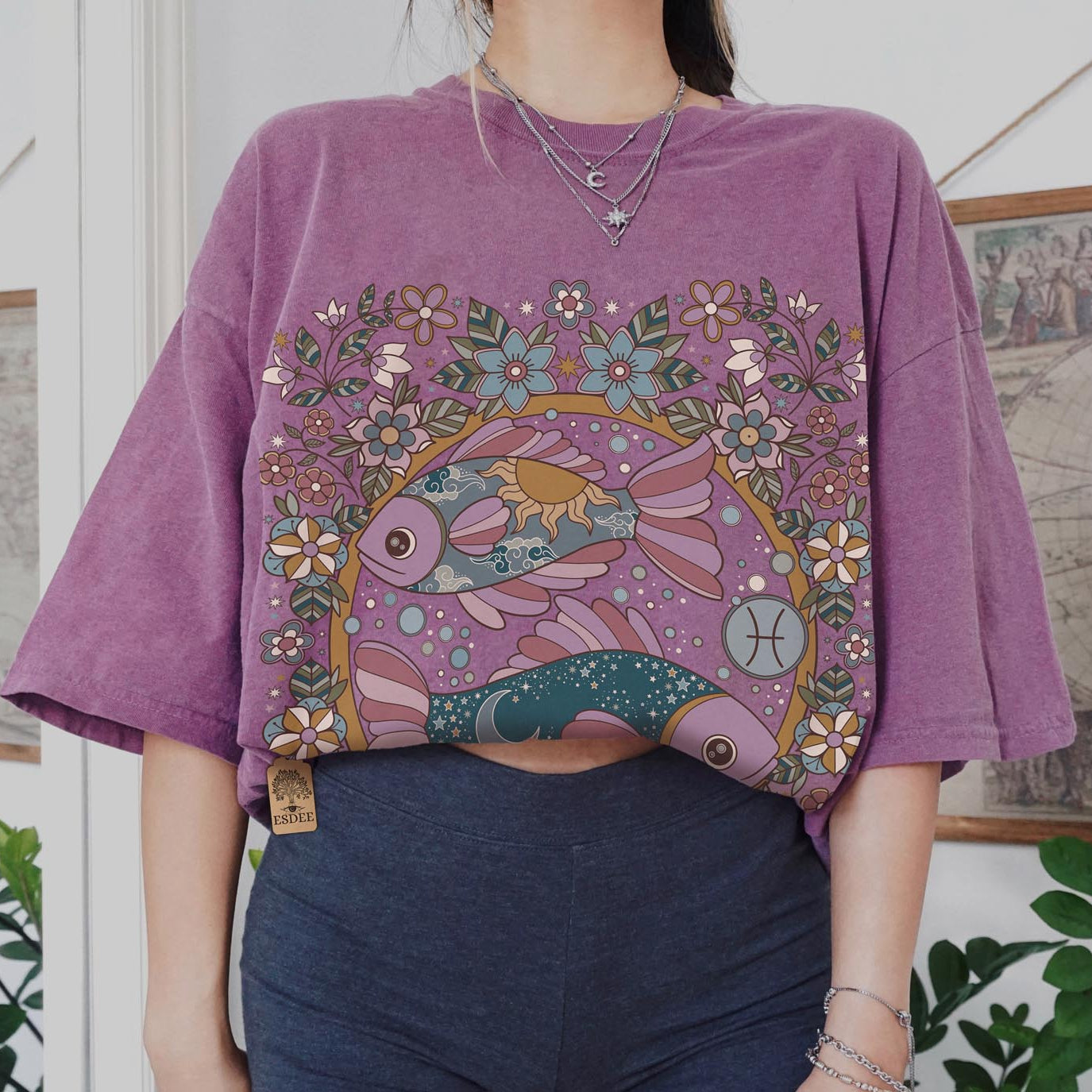 Person wearing a purple t-shirt with a colorful fish design in a room with plants and framed pictures.