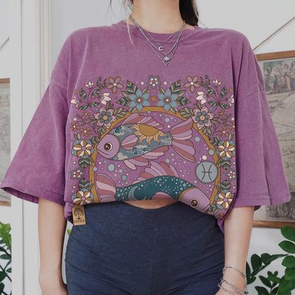 Person wearing a purple t-shirt with a colorful fish design in a room with plants and framed pictures.