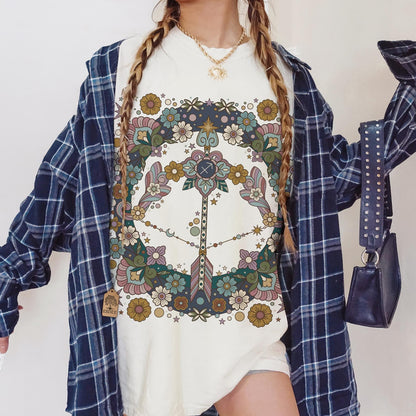 Person wearing a white t-shirt with a colorful design, blue plaid shirt, and holding a purple handbag.